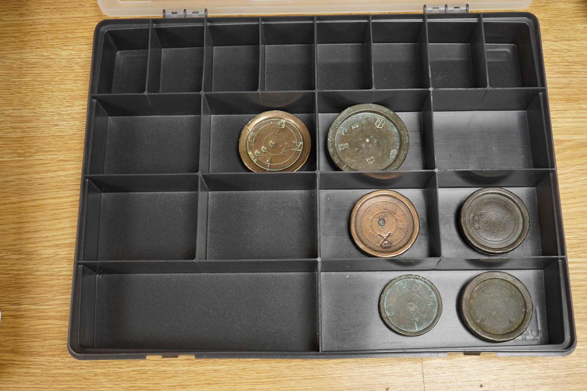 A collection of 16th century to 19th century bronze and lead circular trade weights, stamped with Royal Cyphers, weights, proof marks, the assay dagger for London, etc., contained within four plastic collector’s trays